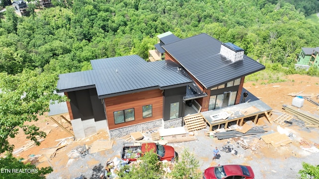 rear view of property with a wooded view, stone siding, a standing seam roof, and metal roof