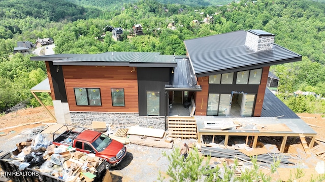 view of front of house with a forest view, stone siding, metal roof, and a wooden deck
