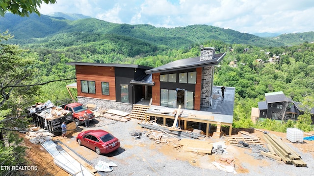 rear view of property with a mountain view, a view of trees, a chimney, and stone siding