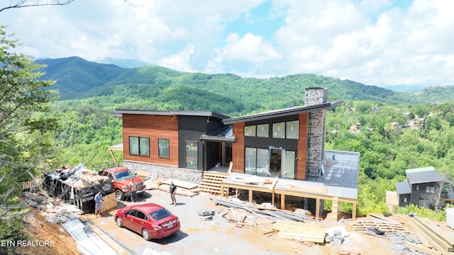 rear view of house with a mountain view, a chimney, a wooded view, and stone siding