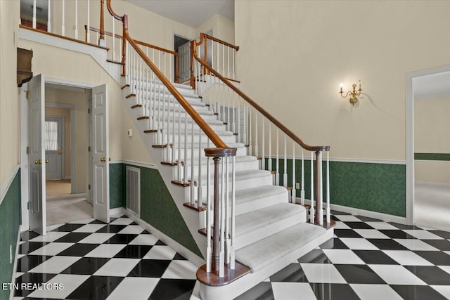 stairs with tile patterned floors, a wainscoted wall, baseboards, and a towering ceiling