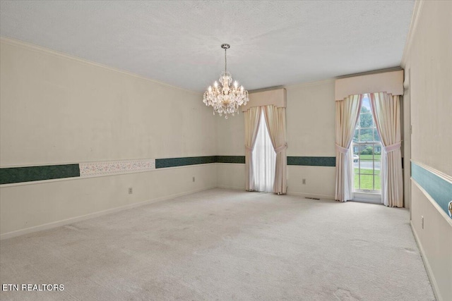 carpeted spare room with a chandelier, ornamental molding, a textured ceiling, and baseboards
