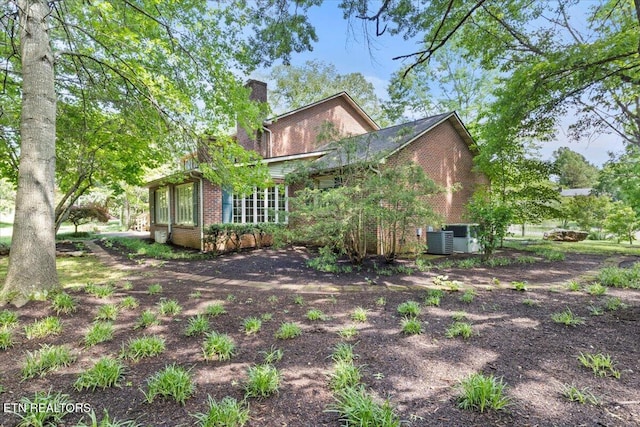 rear view of property featuring brick siding, a chimney, and central AC