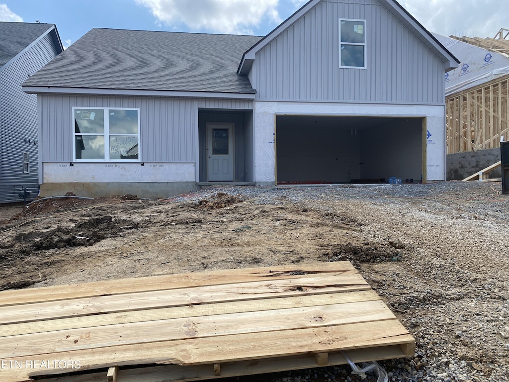 view of front facade featuring roof with shingles and dirt driveway