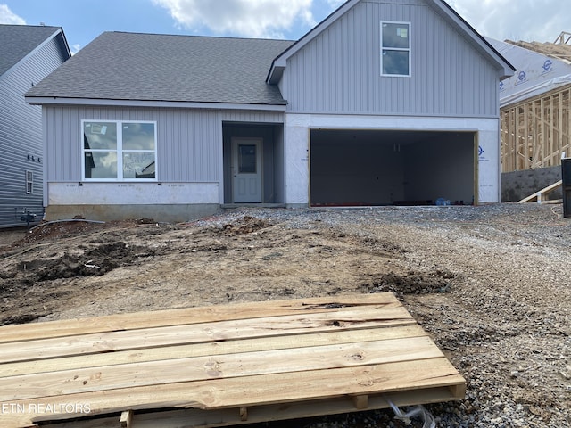 view of front facade featuring roof with shingles and dirt driveway