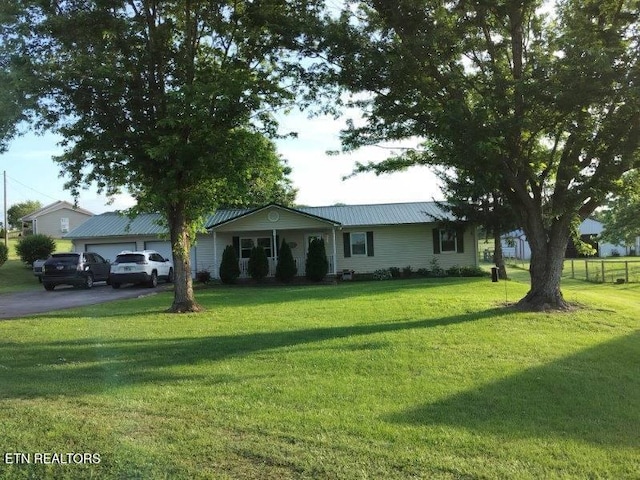 ranch-style home featuring a front lawn, driveway, metal roof, and a detached garage