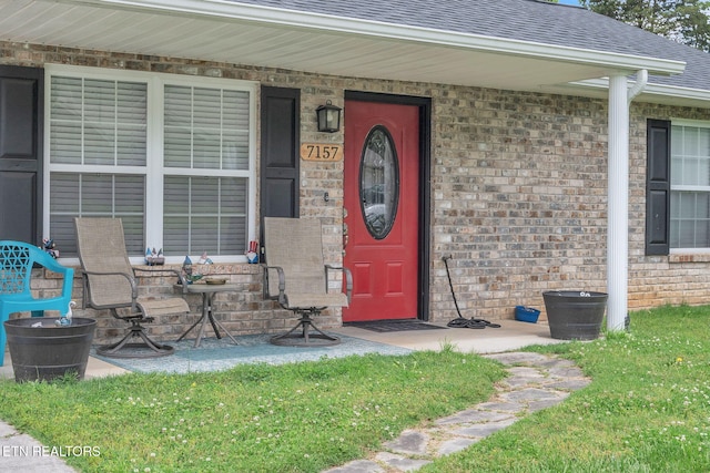 entrance to property featuring roof with shingles, brick siding, and a porch