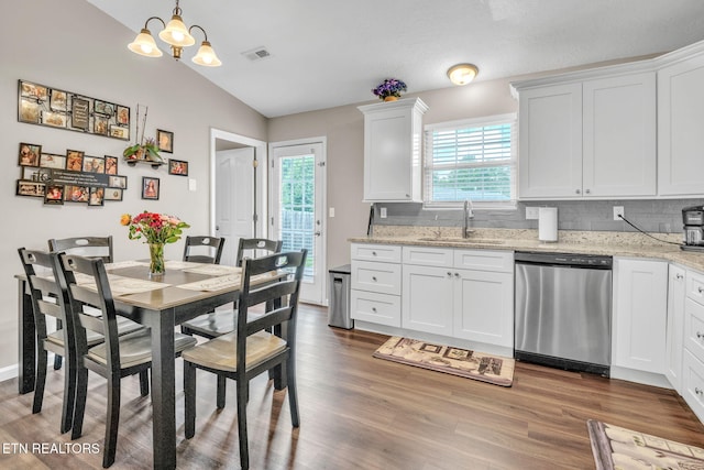 kitchen with stainless steel dishwasher, a sink, lofted ceiling, wood finished floors, and tasteful backsplash