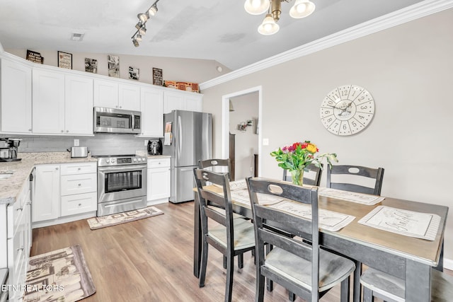 kitchen with stainless steel appliances, lofted ceiling, tasteful backsplash, ornamental molding, and light wood-type flooring