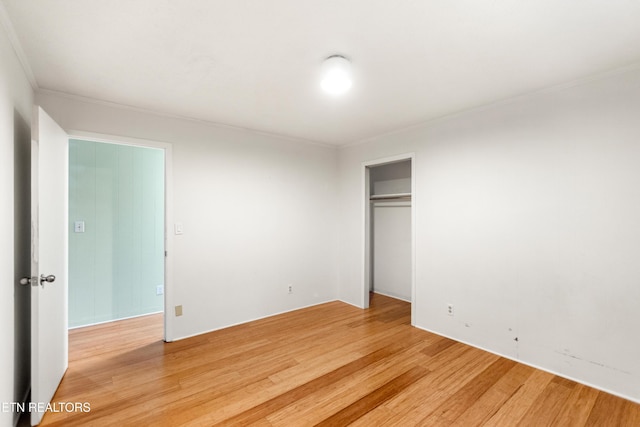 unfurnished bedroom with light wood-style flooring, crown molding, and a closet