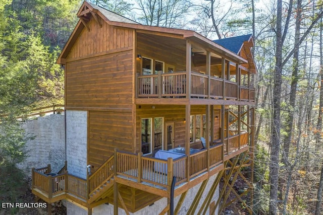 back of property with roof with shingles, a balcony, a wooden deck, and a wooded view