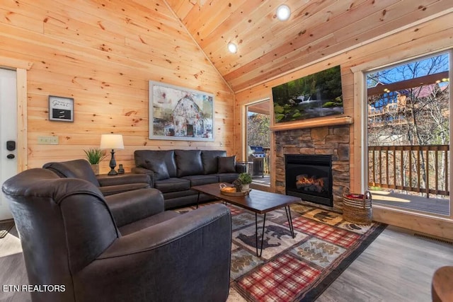 living area with wooden ceiling, vaulted ceiling, wood finished floors, a stone fireplace, and wood walls