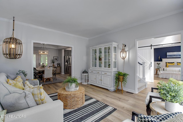 living room with a barn door, crown molding, light wood finished floors, stairs, and a chandelier