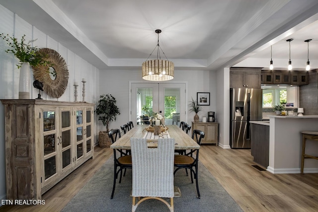 dining area with a raised ceiling, french doors, a chandelier, and light wood-style flooring