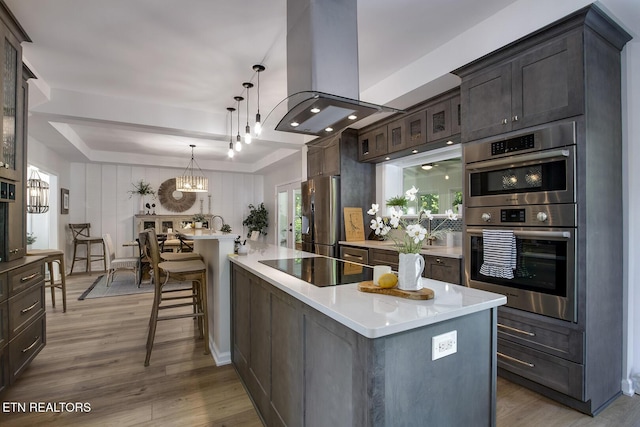 kitchen featuring island exhaust hood, appliances with stainless steel finishes, light countertops, dark brown cabinets, and wood finished floors