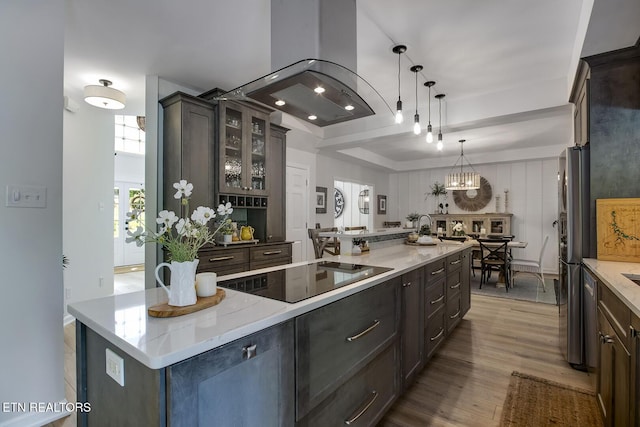 kitchen featuring black electric cooktop, wood finished floors, glass insert cabinets, light stone countertops, and hanging light fixtures