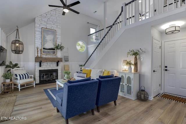 living area with high vaulted ceiling, a ceiling fan, wood finished floors, a wainscoted wall, and stairway