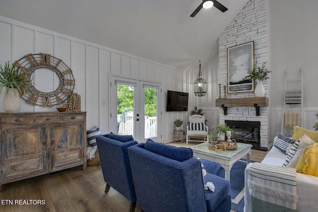 living area with a decorative wall, hardwood / wood-style flooring, ceiling fan, high vaulted ceiling, and a stone fireplace