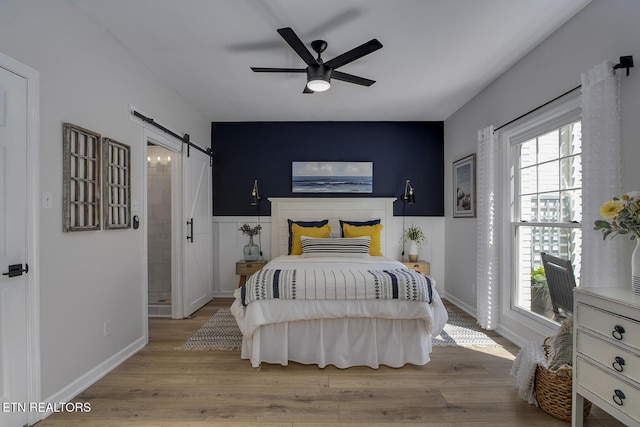 bedroom featuring a barn door, wood finished floors, baseboards, and a ceiling fan