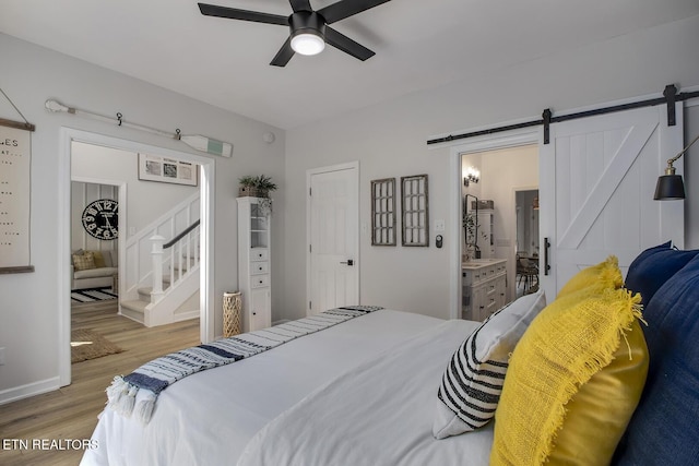 bedroom with a barn door, wood finished floors, baseboards, a ceiling fan, and ensuite bath