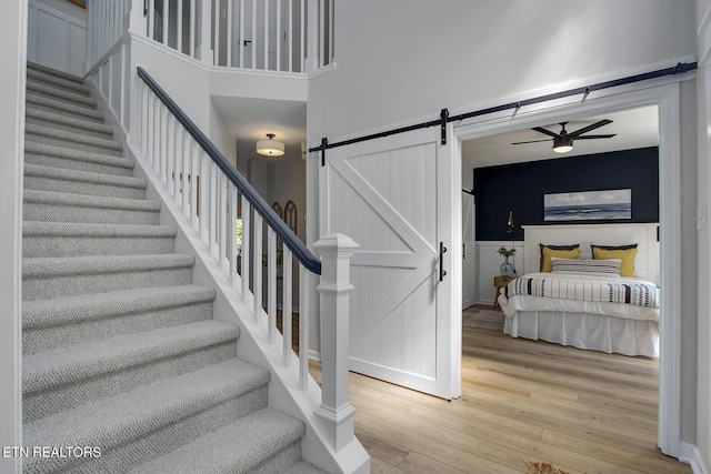 stairs with a barn door, wood finished floors, and a ceiling fan