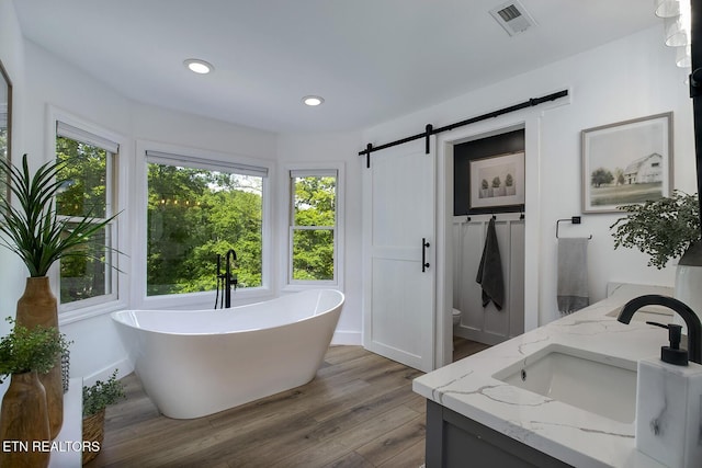 full bath with wood finished floors, a freestanding bath, toilet, vanity, and recessed lighting