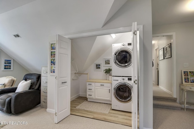 clothes washing area with estacked washer and dryer, light carpet, and baseboards