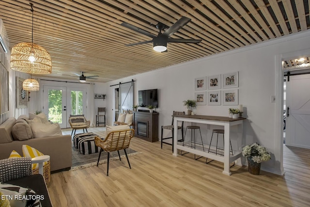 living area featuring a barn door, ceiling fan, french doors, and wood finished floors