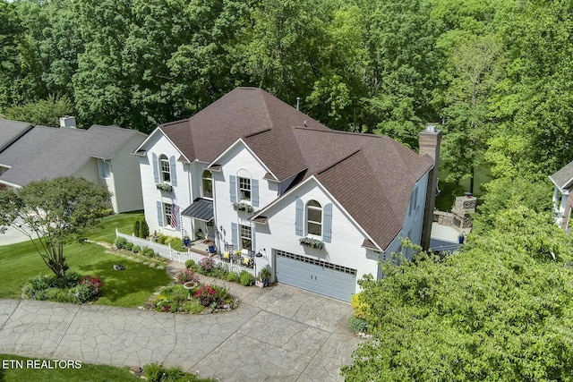 view of front of house with an attached garage, driveway, a chimney, a front lawn, and roof with shingles