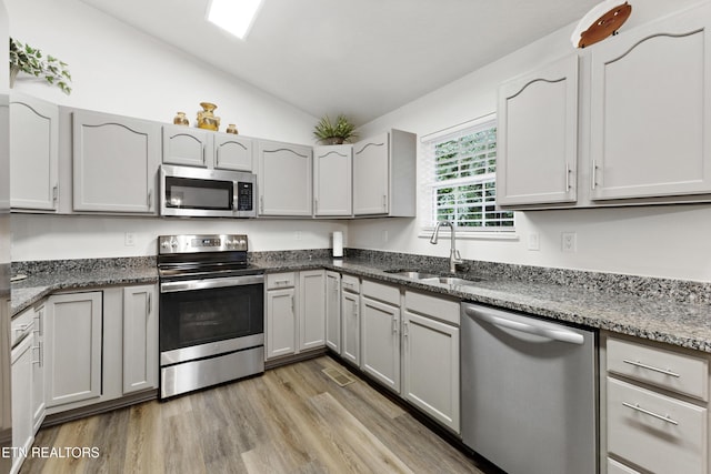 134 Jordan Dr, Caryville, TN 37714 - kitchen featuring appliances with stainless steel finishes, a sink, vaulted ceiling, dark stone countertops, and light wood-type flooring
