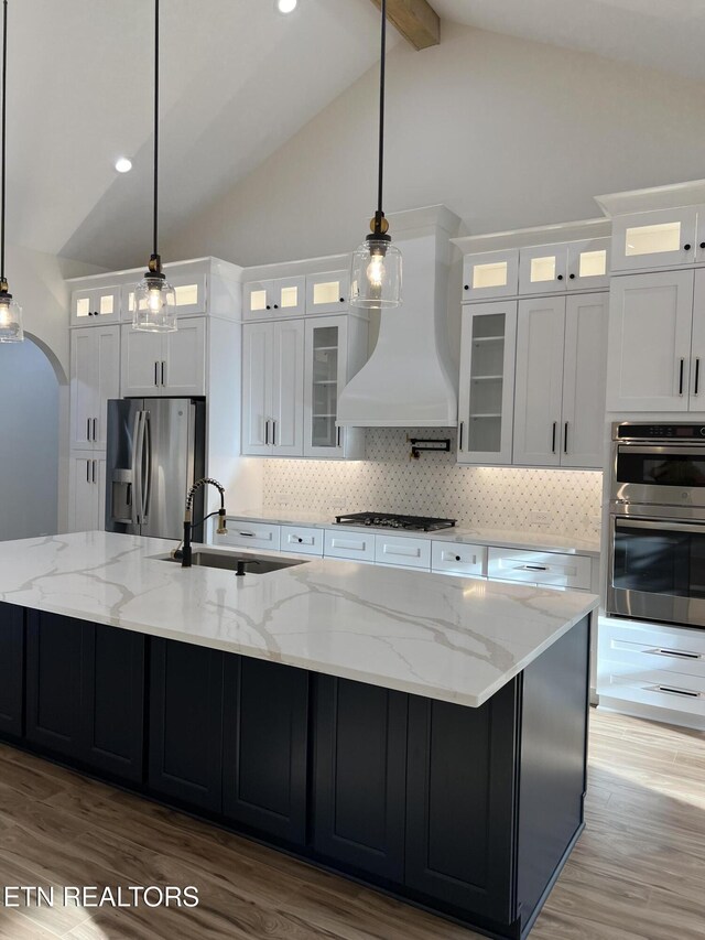 kitchen featuring stainless steel appliances, custom exhaust hood, a sink, beam ceiling, and a spacious island