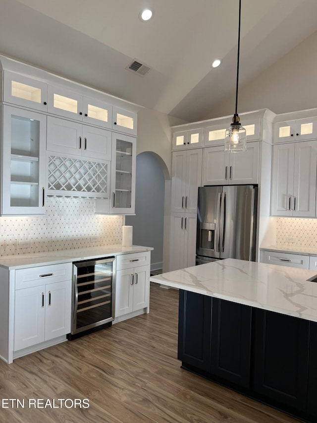 kitchen featuring wine cooler, stainless steel fridge with ice dispenser, arched walkways, backsplash, and light stone counters
