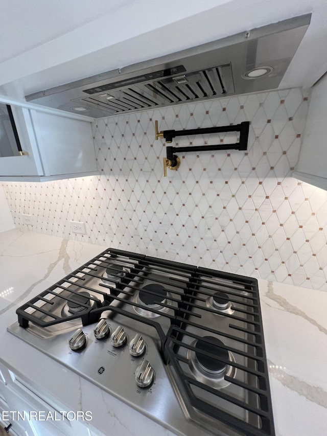 kitchen view of pot filler, stainless steel gas stovetop, tasteful backsplash, and light stone counters