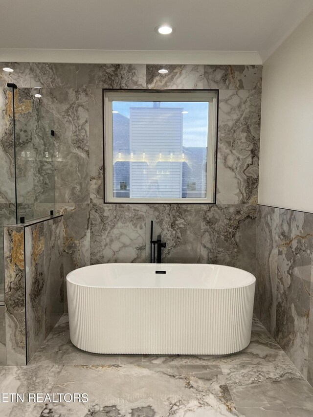 full bath featuring marble tiled floors, a soaking tub, walk in shower, tile walls, and crown molding