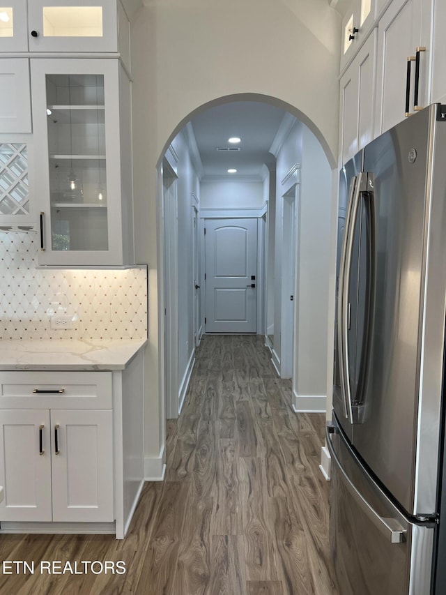 kitchen featuring freestanding refrigerator, dark wood-style floors, arched walkways, white cabinetry, and crown molding