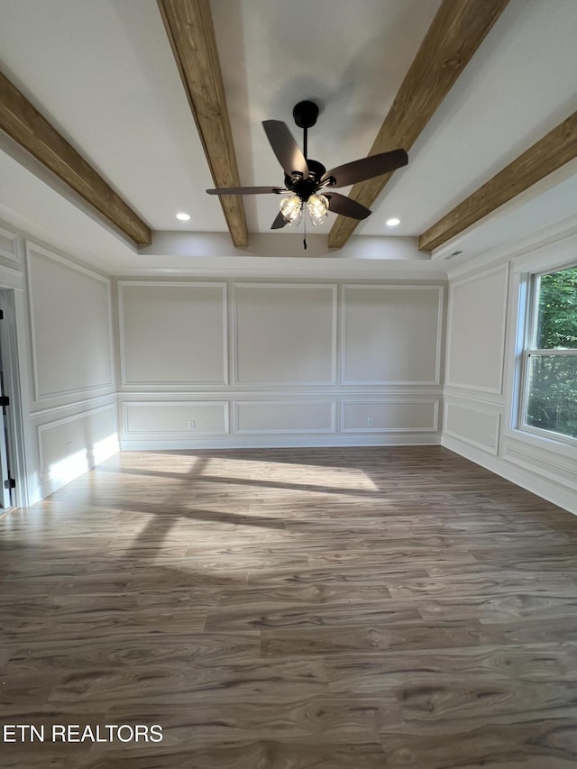 empty room featuring a decorative wall, beamed ceiling, wood finished floors, and ceiling fan