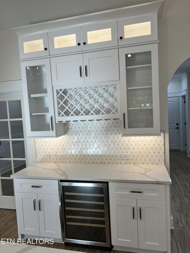 indoor dry bar featuring wine cooler, arched walkways, decorative backsplash, and dark wood finished floors