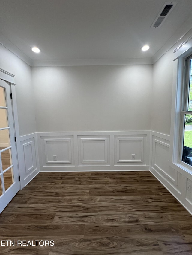 empty room featuring dark wood finished floors, a decorative wall, ornamental molding, and a wainscoted wall