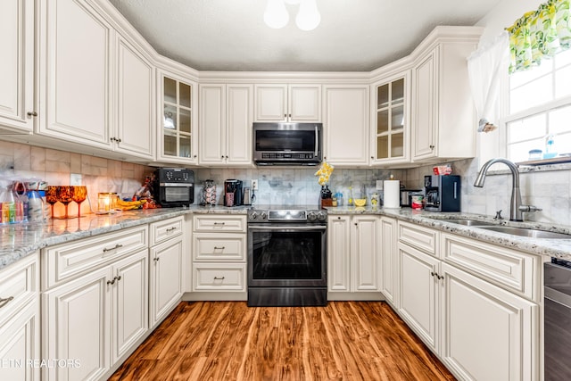 kitchen featuring appliances with stainless steel finishes, a sink, white cabinets, light wood finished floors, and glass insert cabinets