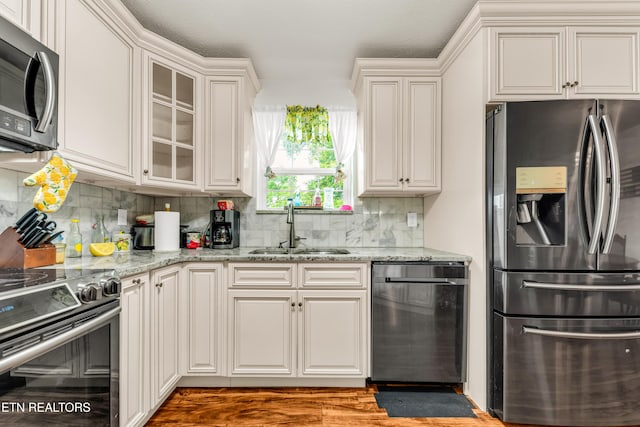 kitchen featuring stainless steel appliances, a sink, decorative backsplash, light stone counters, and wood finished floors