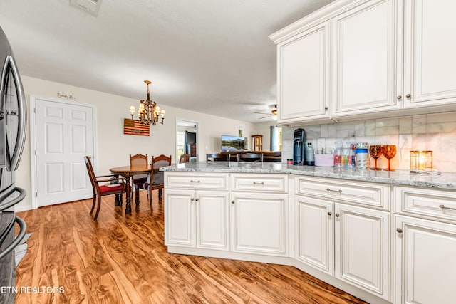 kitchen featuring a chandelier, stainless steel refrigerator with ice dispenser, a peninsula, light wood-style floors, and white cabinetry