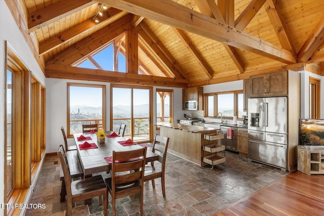 dining area featuring wood ceiling, beamed ceiling, stone tile floors, and high vaulted ceiling