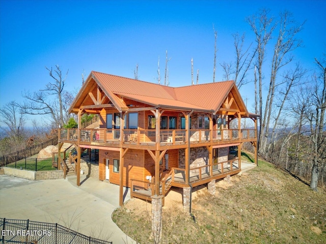 back of house featuring fence, a wooden deck, concrete driveway, and metal roof