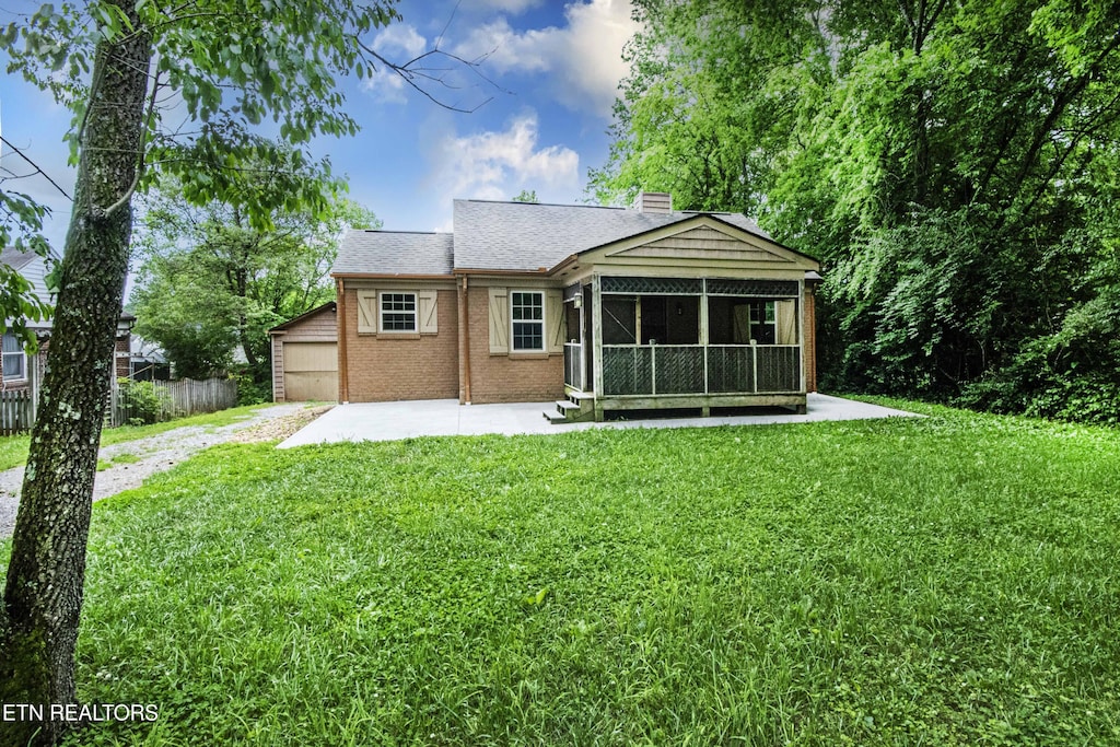 back of property featuring a sunroom, a chimney, brick siding, a garage, and driveway