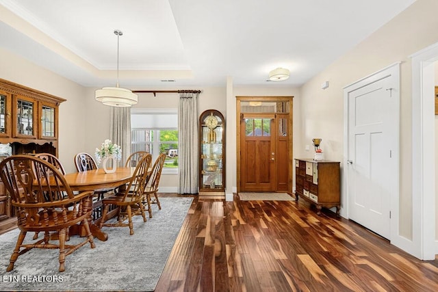 dining space featuring wood finished floors, a tray ceiling, baseboards, and crown molding