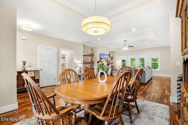 dining area with a raised ceiling, dark wood-style flooring, ornamental molding, ceiling fan, and baseboards