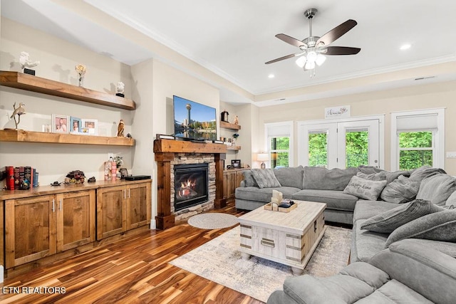 living room featuring wood finished floors, crown molding, a ceiling fan, a fireplace, and a tray ceiling