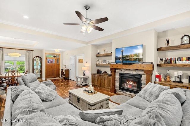 living room with a raised ceiling, wood finished floors, ceiling fan, crown molding, and a fireplace
