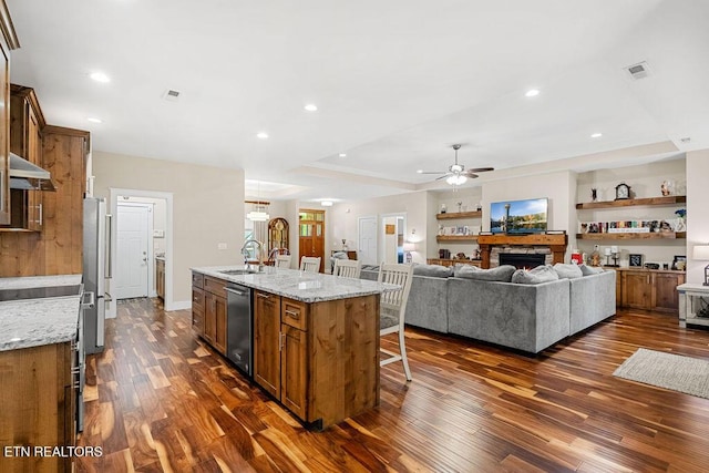 kitchen with stainless steel appliances, a ceiling fan, dark wood-style flooring, brown cabinetry, and a breakfast bar area