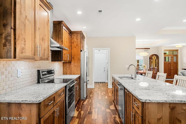 kitchen with appliances with stainless steel finishes, brown cabinetry, a sink, an island with sink, and recessed lighting